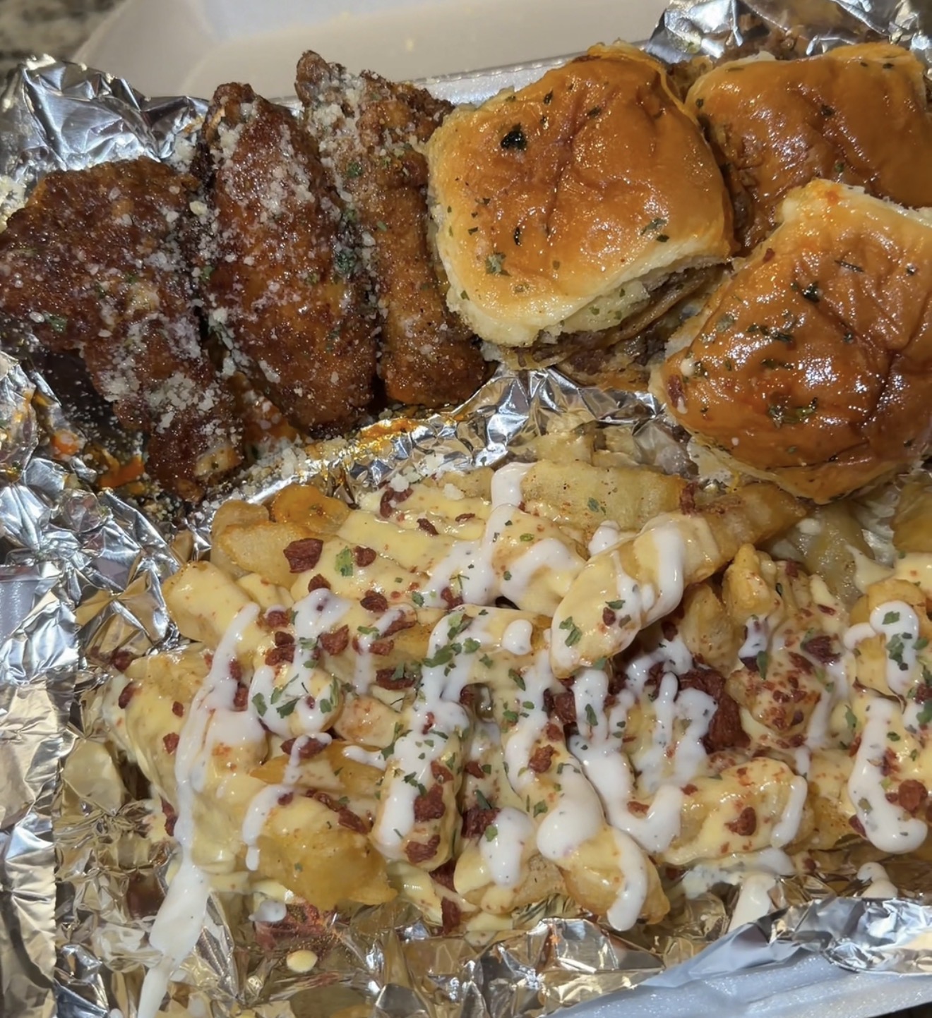 Platter of glazed wings, cheeseburger sliders and loaded fries
